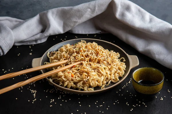 Delicious noodles with sesame seeds, teriyaki, a sauce, and chopsticks on black background