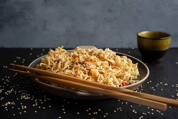 Delicious noodles with sesame seeds, teriyaki, a sauce, and chopsticks on black background