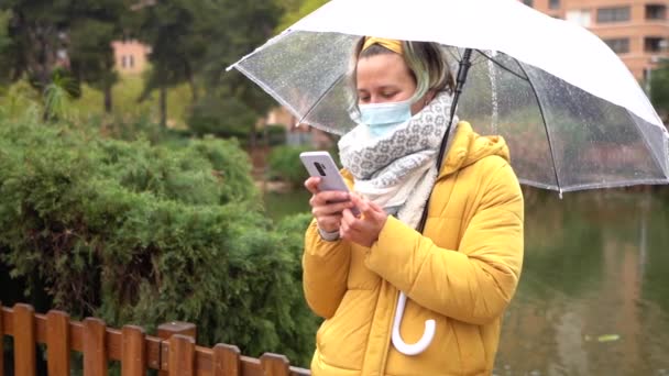 Een Lachende Spaanse Vrouw Typt Haar Telefoon Houdt Een Paraplu — Stockvideo