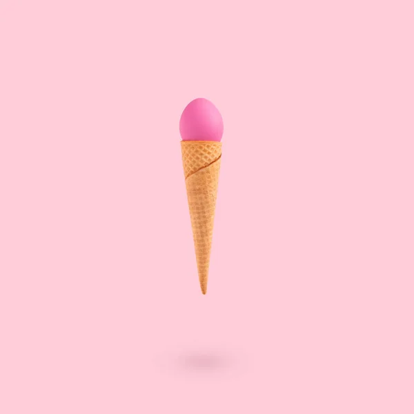 A vertical shot of a pink egg on an ice cream cone on a pink background