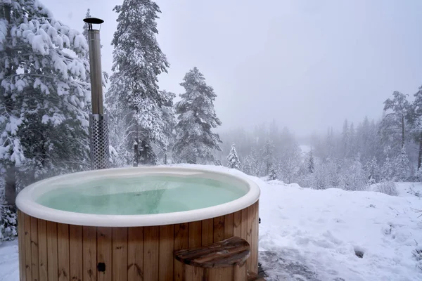 A wooden hot tub  near a winter forest on a snowy day,   Kroderen, Norway