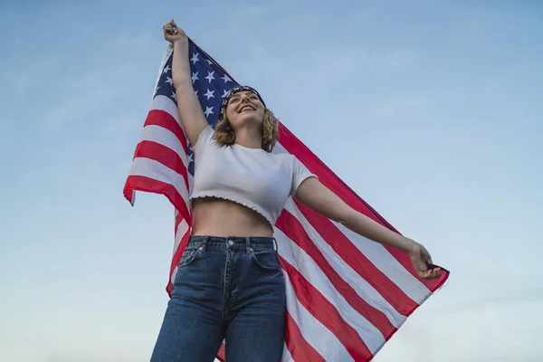 一位年轻的白人女性 在蓝天的映衬下高举美国国旗 — 图库照片