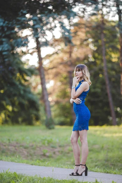 公園でポーズをとっているエレガントな青のドレスを着た若いブロンドの女性の垂直ショット — ストック写真