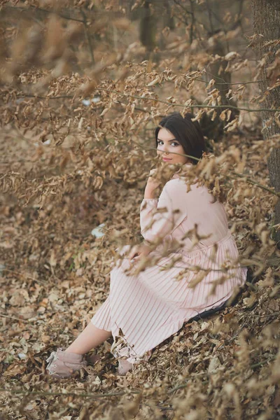 一位年轻的高加索女性 身穿精致的粉色连衣裙 坐在森林里枯干的树上 — 图库照片