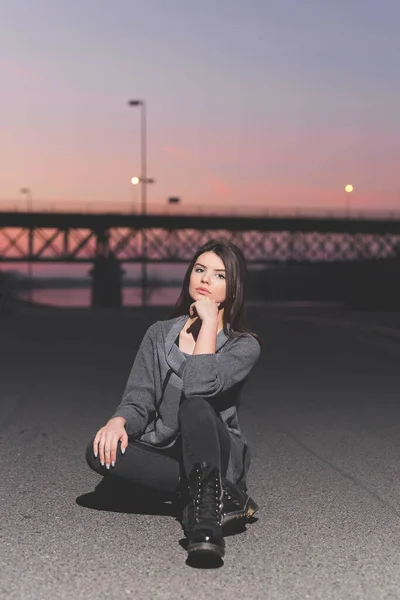 一个年轻的高加索女人在日落时坐在路上的一张垂直的照片 — 图库照片