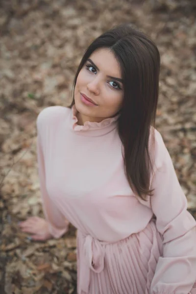 一幅年轻女子穿着精致的粉色连衣裙坐在森林枯树上的画像 — 图库照片