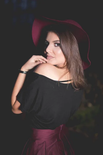 一个穿着勃艮第短裙 头戴帽子 头戴深色背景的年轻女性的竖直照片 — 图库照片
