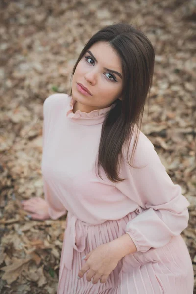 在森林里 一个身穿华丽粉色连衣裙的年轻的高加索女人坐在地上的一张垂直的照片 — 图库照片
