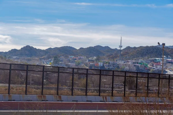 A border wall with Mexico paralleling a street and railroad tracks