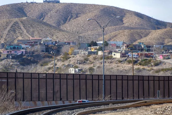 A border wall with Mexico paralleling a street and railroad tracks