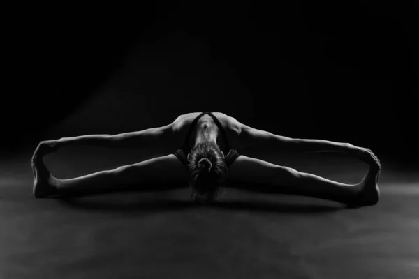 一个穿着运动服的女人在黑暗背景的工作室里做瑜伽的灰度照片 — 图库照片