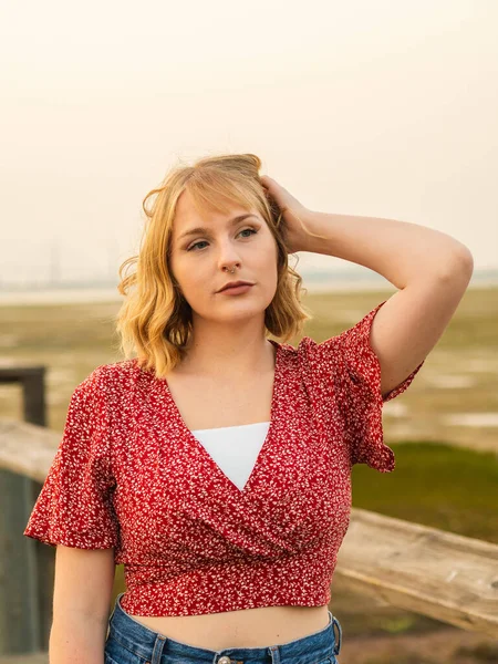 一位年轻的金发女子穿着一件红色的装饰过的衬衫 站在室外摆姿势 — 图库照片