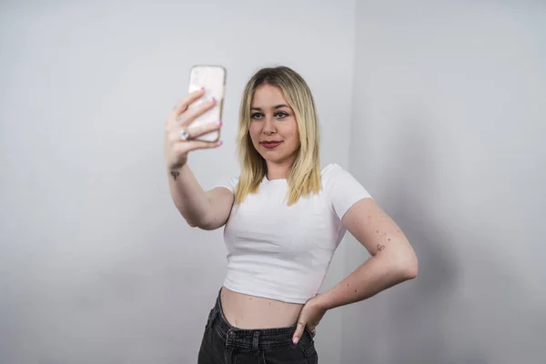 一位年轻的白人女性 来自西班牙 拿着手机靠着白墙自拍 — 图库照片