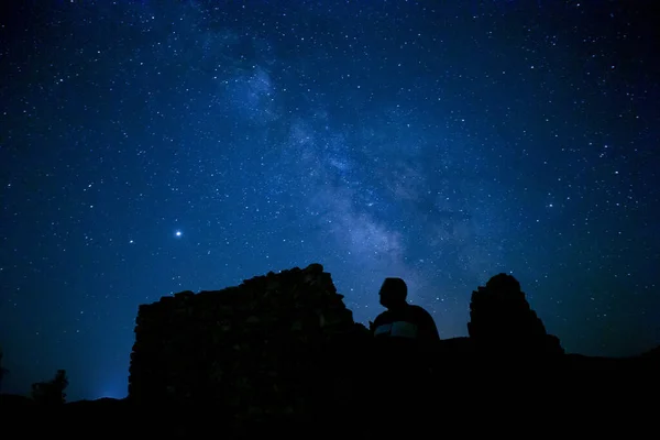 星空を眺めながら崖の上に座っている男のシルエットの魔法の景色 — ストック写真