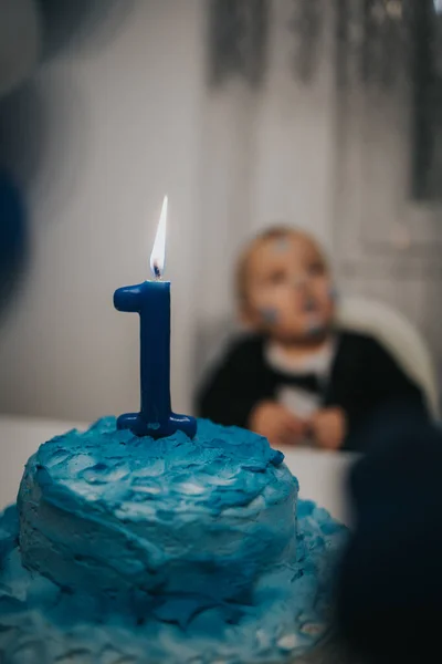 ぼやけた子供の背景に青いケーキの上に炎を持つ数1キャンドルの選択的な焦点 — ストック写真