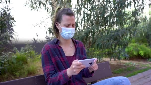 Hdで公園でビデオゲームをプレイしながら顔マスクを身に着けているスペイン人女性のスローモーション — ストック動画