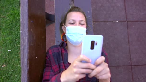 Hdでテキストメッセージをしながら ベンチに横に顔のマスクを身に着けているスペイン人女性のスローモーション — ストック動画
