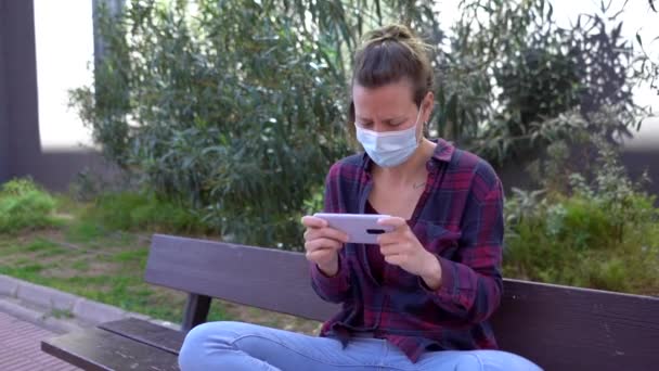 Hdで公園でビデオゲームをプレイしながら顔マスクを身に着けているスペイン人女性のスローモーション — ストック動画