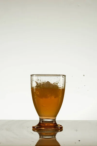 反射面に氷が隔離された黄色の飲み物のガラスの垂直ショット — ストック写真