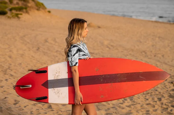 一个年轻的金发女冲浪手和她的冲浪板在海滩上散步 — 图库照片