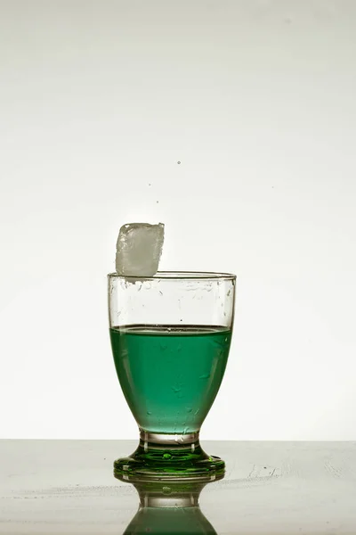 Крижаний Куб Падає Склянку Зеленого Напою Ізольовано Відбиваючій Поверхні — стокове фото