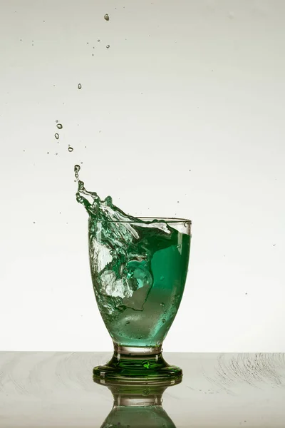 Yansıtıcı Yüzeyde Izole Edilmiş Yeşil Bir Bardak Sıçratan Bir Içki — Stok fotoğraf