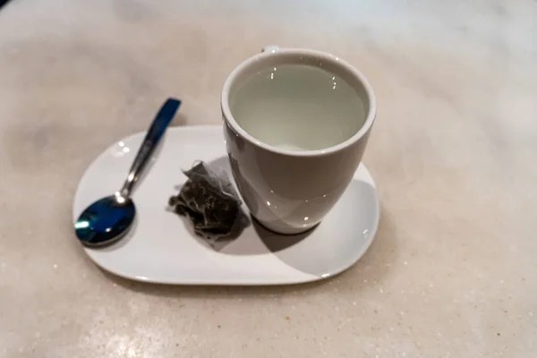 Высокоугольный Снимок Чашки Горячей Воды Ложкой Пакетиком Чая Белой Тарелке — стоковое фото
