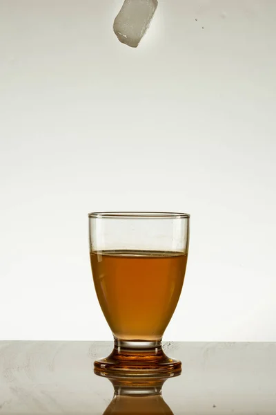 Cubo Gelo Que Cai Num Copo Bebida Amarela Isolado Superfície — Fotografia de Stock