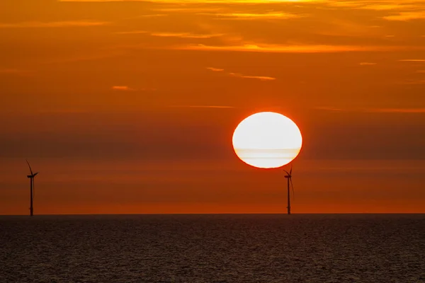 夕阳西下的时候 北海上有两个风力涡轮机 在太阳前面 天空一片红晕 — 图库照片