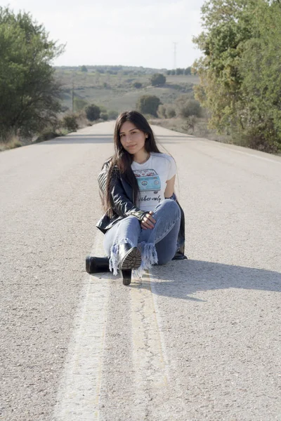 一名年轻的拉丁女子穿着牛仔裤 紧身衣和皮夹克 在沥青路面上摆姿势 — 图库照片