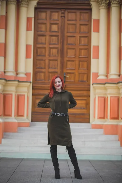建物の前に立つ緑のドレスに赤い髪をした魅力的な若い白人女性 — ストック写真
