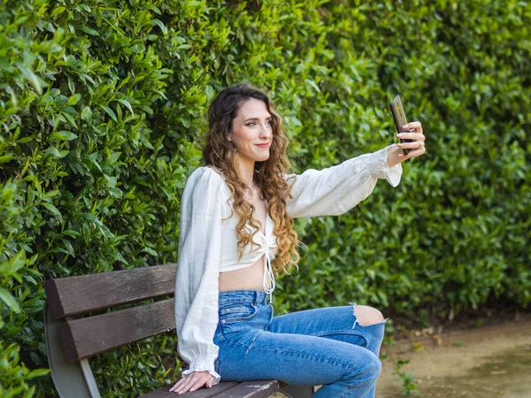 Stylowa Młoda Hiszpanka Robi Sobie Selfie Siedząc Ławce Wiosennym Parku — Zdjęcie stockowe