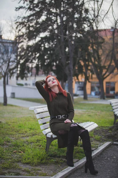 公園のベンチにポーズをとる赤い髪の若い女性の垂直ショット — ストック写真