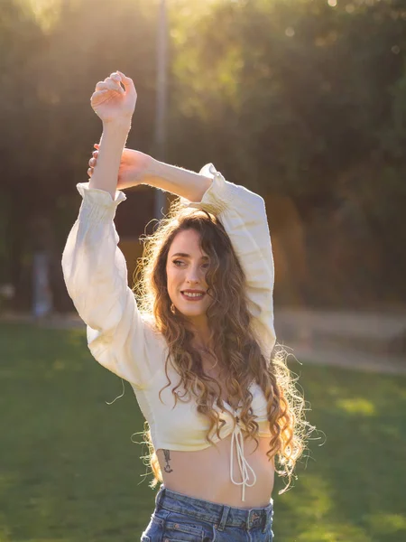 春の天気を楽しむかなり長い髪のスペインの女の子 モデルは晴れた日に公園で彼女の腕を上げてポーズをとっています — ストック写真
