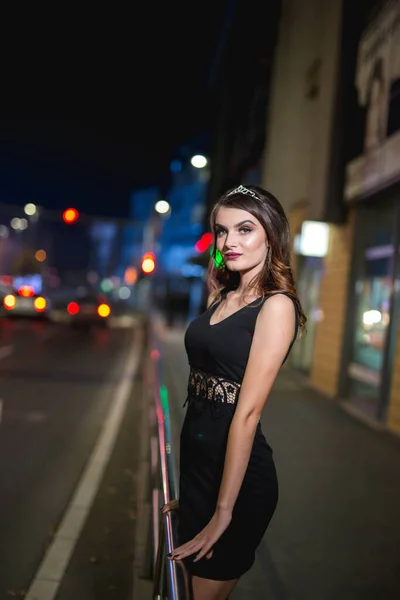 夜に歩道にポーズをとるエレガントな黒のドレスで若い女性モデルの垂直ショット — ストック写真