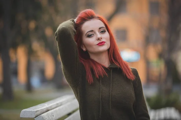 在公园的长椅上摆姿势的红头发年轻女子的画像 — 图库照片