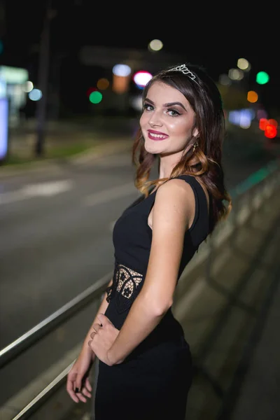 一张年轻女模特穿着典雅的黑色连衣裙夜间在人行道上摆姿势的纵向照片 — 图库照片