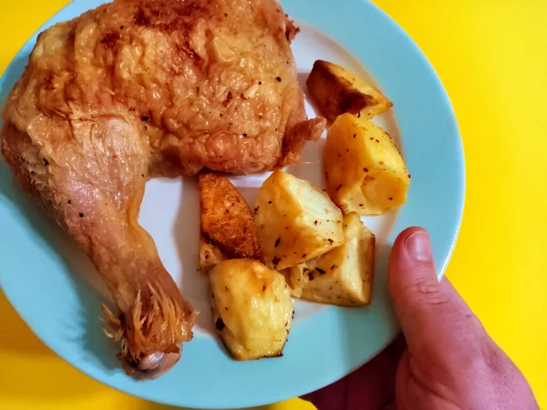 一只手拿着盘子的头顶拍摄的照片 盘子里有传统的烤鸡腿和烤西班牙土豆 黄色背景 — 图库照片