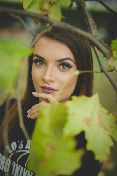 公園で緑の葉を持つ木の近くにポーズ若いブルネット白人女性 — ストック写真