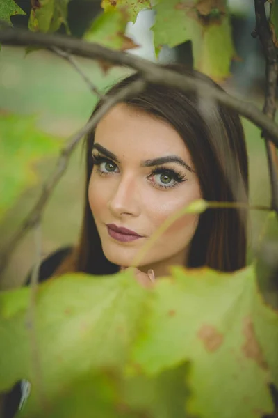 公園で緑の葉を持つ木の近くにポーズ若いブルネット白人女性 — ストック写真