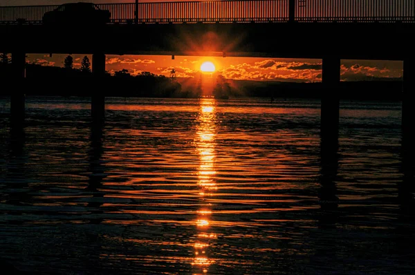 一个迷人的橙色落日镜头掠过一条河和一座桥 — 图库照片