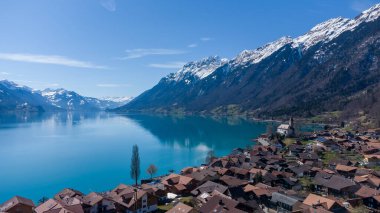 A landscape of a lake surrounded by rocky hills and buildings in Brienz, Switzerland clipart