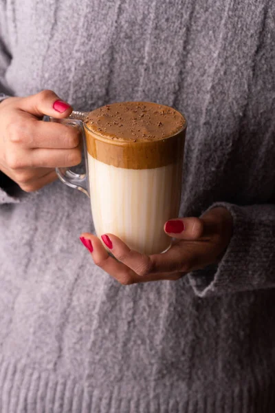 クリーム色のダルゴナコーヒーのガラスを保持ウールセーターの女性の垂直ショットはチョコレートで振りかけ — ストック写真