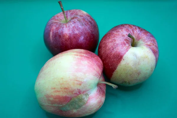 A closeup shot of a group of three abstract apples on a green background - red apple with a streak of green