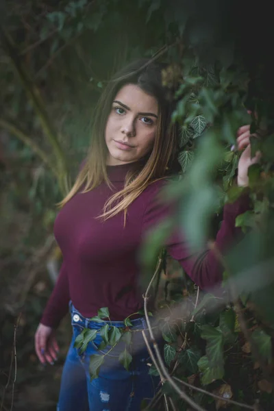 一位身穿紫色假脖子毛衣的年轻貌美女子在公园的灌木丛中出现 她的目光浅浅的 — 图库照片