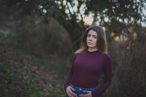濃い緑に対して屋外でポーズ紫色のモックネックセーターでかなり若い女性の浅い焦点 — ストック写真