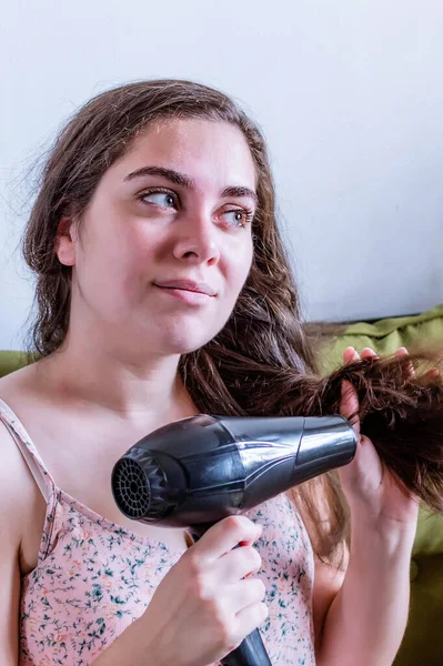 A vertical shot of a young Jewish woman drying her hair with a blow dryer
