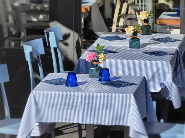 A line of cute square tables with patterned blue and white tablecloths and flowers on them