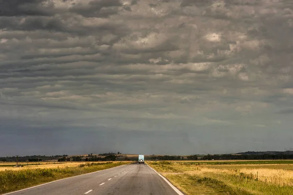 Een Vrachtwagen Weg Omringd Door Lege Velden Onder Bewolkte Hemel — Stockfoto