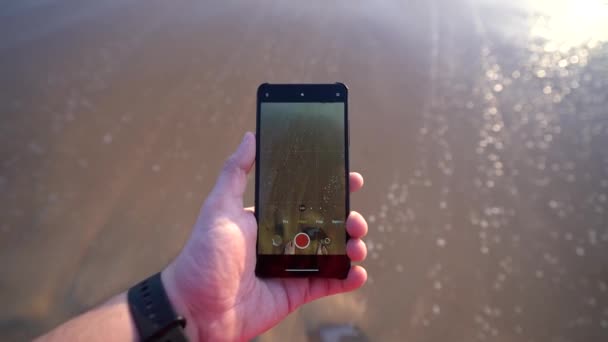 男子手持智能手机 在阳光灿烂的日子拍摄沙滩和波浪大海的视频 — 图库视频影像